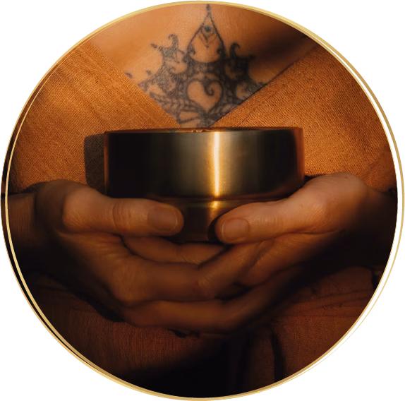 Goldene Cacaoschale wird von zwei Händen gehalten, vor einem spirituellen Brusttattoo in orangener Kleidung.