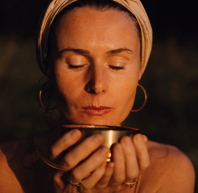 Ava von avaCao mit Turban hält eine goldene Cacaoschale mit geschlossenen Augen vor ihrem Gesicht und genießt achtsam den Moment
