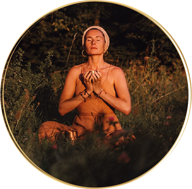 Ava von avaCao sitzt meditierend in der Abendsonne auf einer Wiese, hält eine Schale Cacao