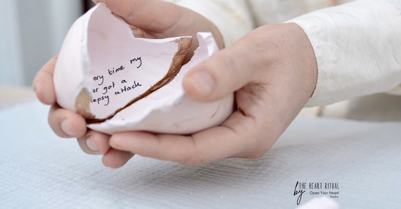 Hände halten ein zerbrochenes Keramikherz mit handgeschriebenem englischen Text im Inneren