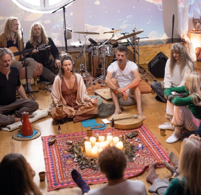 Menschen sitzen im Kreis bei einer Cacao-Zeremonie mit Musik, Kerzen und Instrumenten, spirituelle Projektionen an der Wand