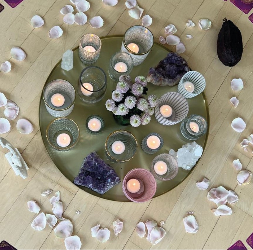 Zeremonieller Altar mit rosa Kerzen, Cacaobohne, Orakelkarten, Kristallen und Rosenblättern