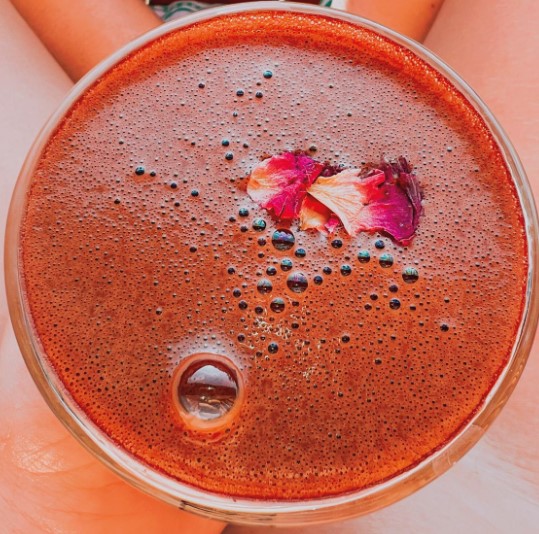 Tasse mit cremigem zeremoniellem Cacao, verziert mit getrockneten Blütenblättern, von Händen gehalten