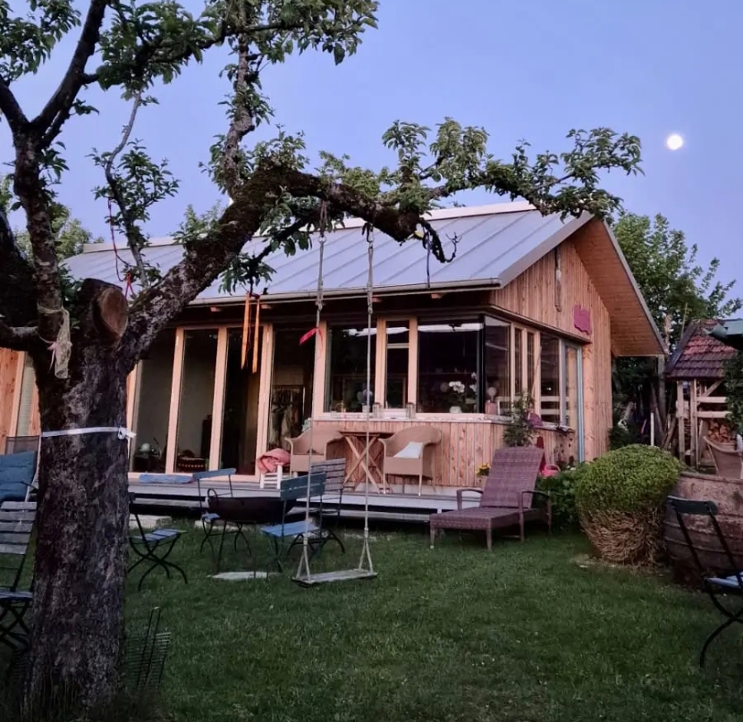 Holzhaus im Garten bei Vollmond. Ava's cacaoHaus ist umgeben von blühender Natur, ein Ort für Rückzug, Herzöffnung und heilsame Cacao-Zeremonien.